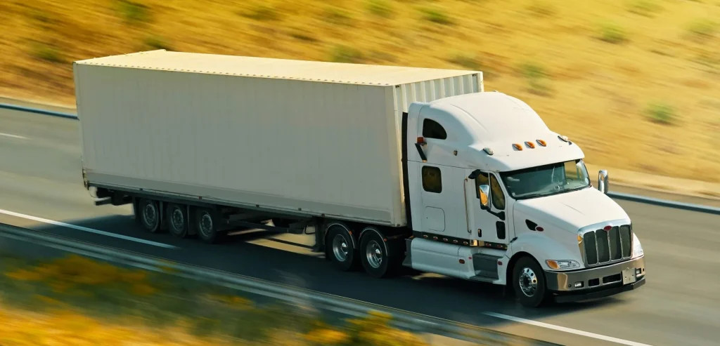 White sleeper semi truck hauling a long 53-foot trailer down an open highway in bright daylight